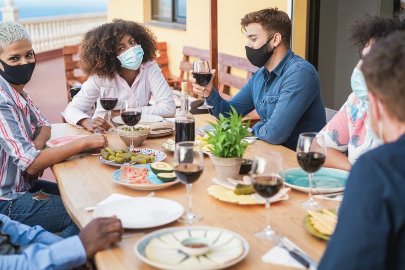 Friends eating and drinking wine together with protective masks.