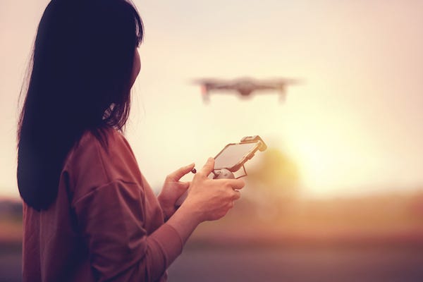 Woman operating a drone with remote control in sunset.