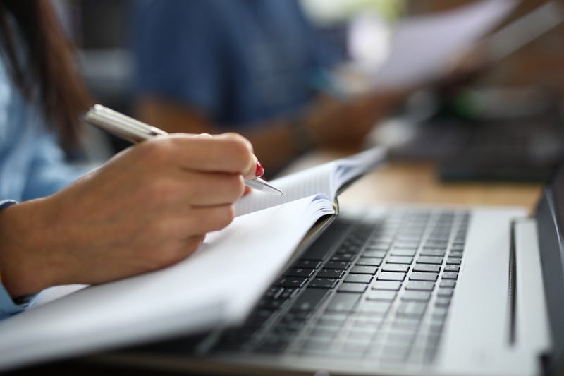 woman writing on paper in front of computer