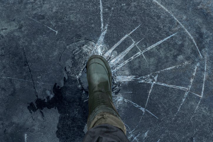 Close up of a man's winter boot pressing on the frozen surface of a lake. The ice is cracking and fracturing under the weight of his step.
