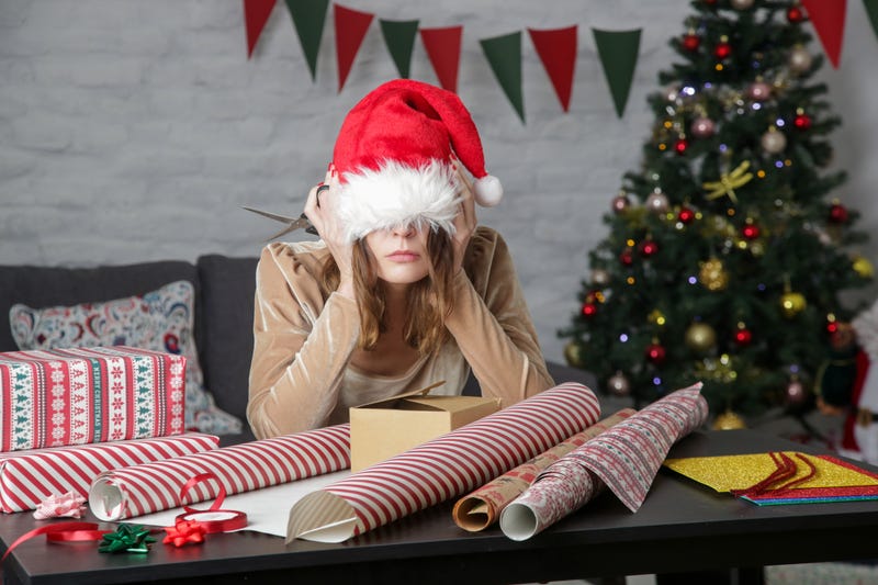 Woman stressed out in santa hat surrounded by wrapping paper
