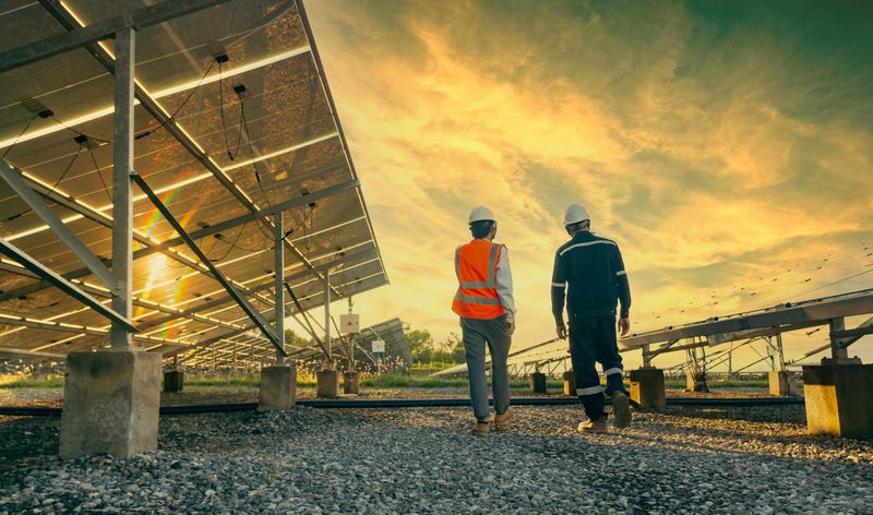 Low angle view of technician walks with investor through field of solar panels, alternative energy to conserve the world's energy