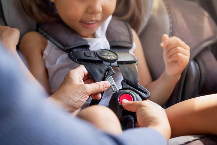 child getting buckled into a car seat
