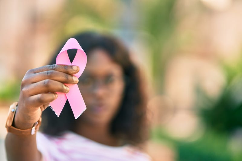 A woman holding a pink ribbon signifying breast cancer.