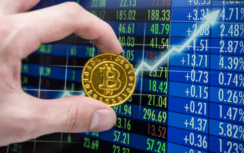 A golden bitcoin coin in front of a stock exchange chart.
