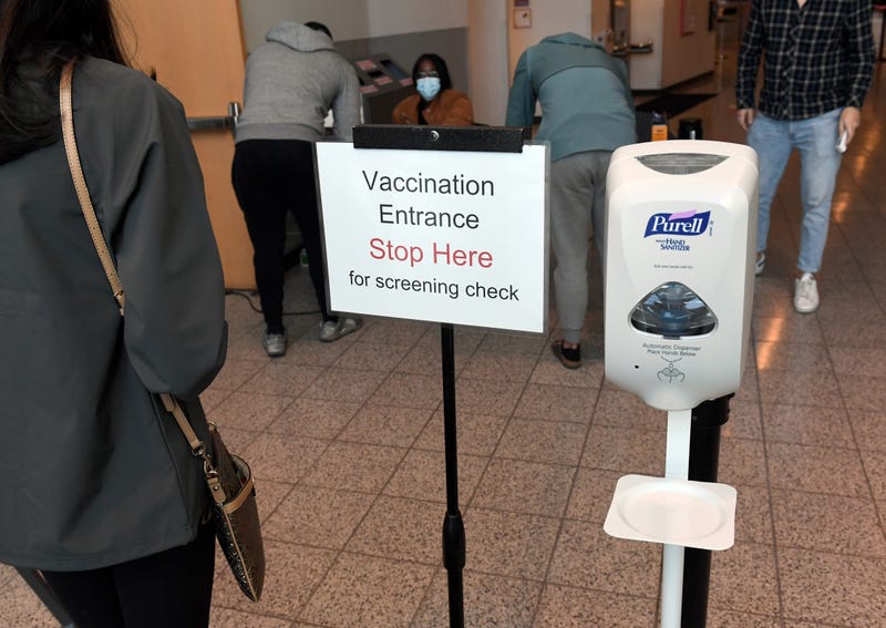 A sign is posted next to a hand sanitizer dispenser at the entrance to a Pfizer-BioNTech COVID-19 vaccination center at UNLV