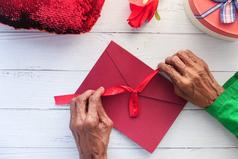 senior woman's hand on red color envelope and gift on table