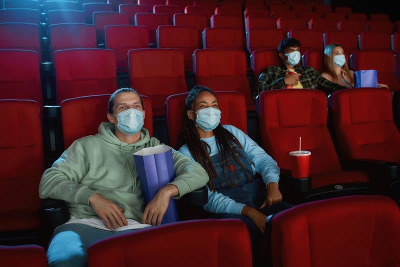 Cheerful young couple wearing face masks for protection from virus disease while watching movie in cinema auditorium. Social distance, entertainment and pandemic concept. 