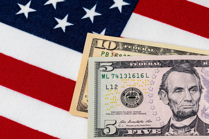 Closeup of ten and five dollar bills with American flag. Concept of 15 dollar federal minimum wage increase.