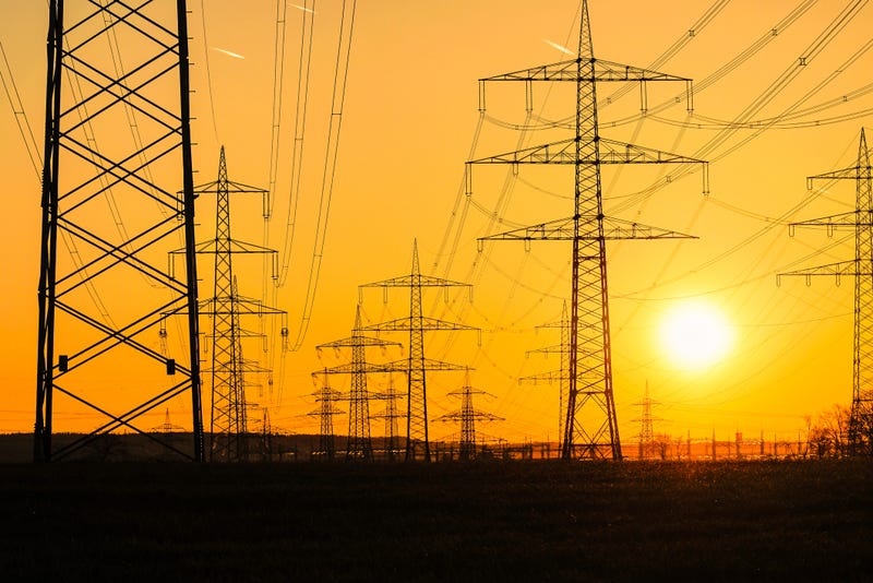 Electricity poles and electric power transmission lines against vibrant orange sky at sunset on a hot day with flickering air. High Voltage towers provide power supply over a long distance. - stock photo