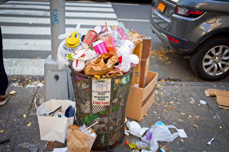 Trash can overflowing with trash on a Manhattan sidewalk.