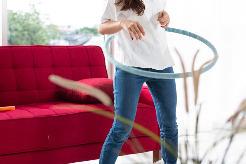 women playing Hula Hoop in the living room at home. Young adult woman learning to play with a hula-hoop in a living room.