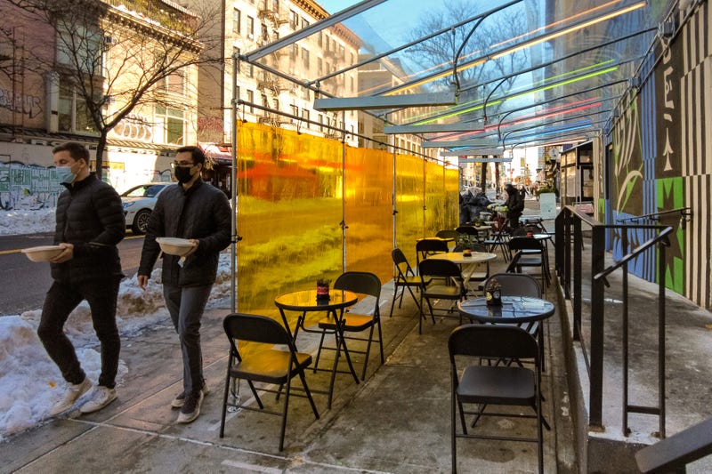 People holding takeout meal orders walk past an outdoor dining area in the Nolita neighborhood of Manhattan during the coronavirus pandemic on Feb. 4, 2021.