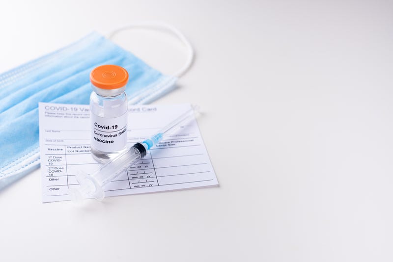 Coronavirus vaccination concept. Covid-19 vaccine vial, vaccination record card, syringe, medical mask on a white background, copy space, close up.