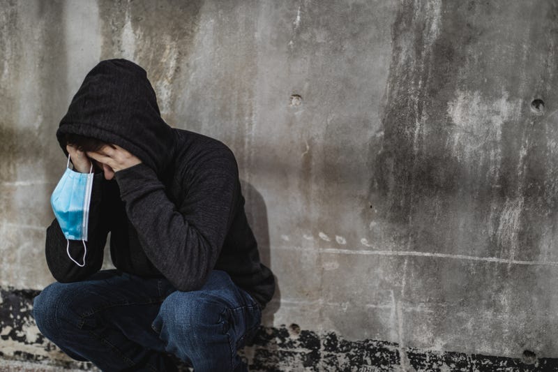 A young man crouches in anguish against a cement wall.