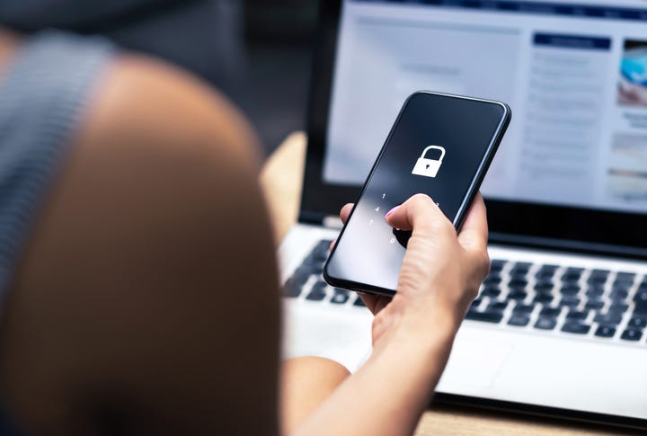 woman holding a cell phone while sitting in front of a laptop