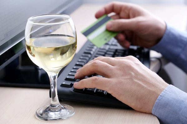 Man typing on a keyboard holding a credit card next to a glass of white wine
