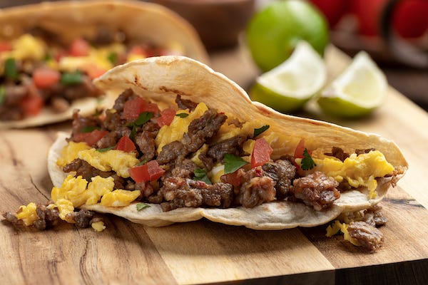 Closeup of a breakfast taco with scrambled egg, sausage and tomato on a wooden cutting board