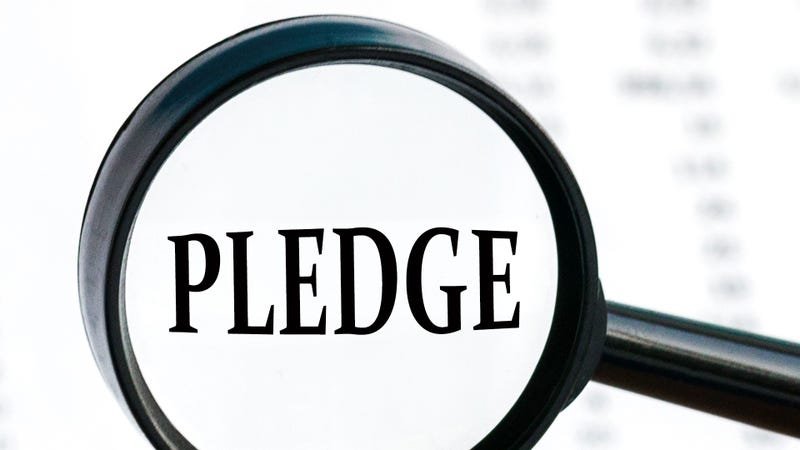 Looking through a magnifying glass at the word Pledge, a business concept