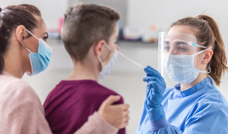 Mom holds her son as medical worker takes sample from his nose during coronavirus pandemic testing.