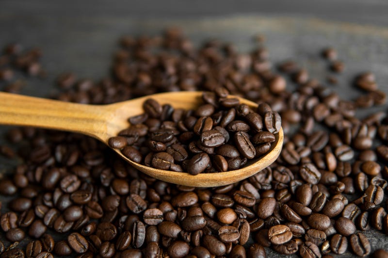 Fresh roasted arabica coffee beans in a wooden spoon and scattered coffee beans on a wooden table