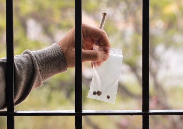 Prisoner’s hand holding joint and a bag of drugs through a jail cell’s bars
