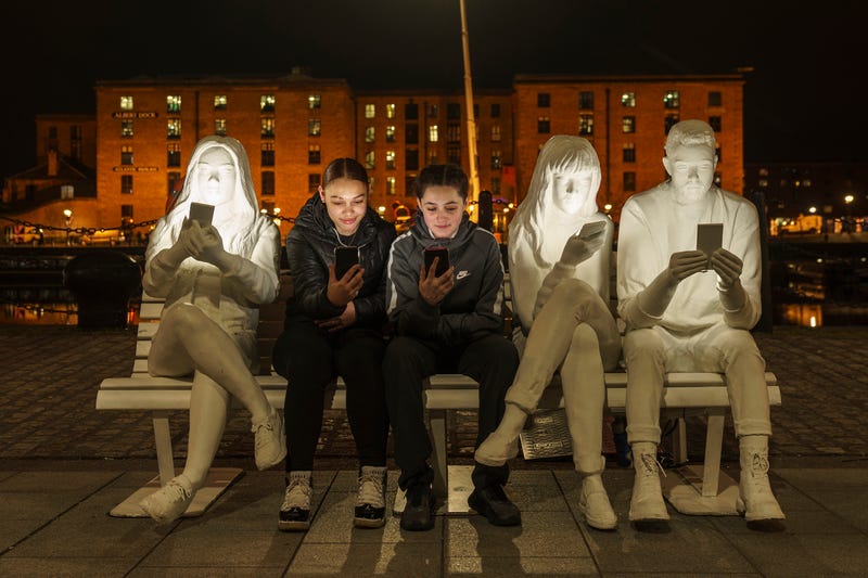 A pair of teens sit with their smartphones in Liverpool, England.