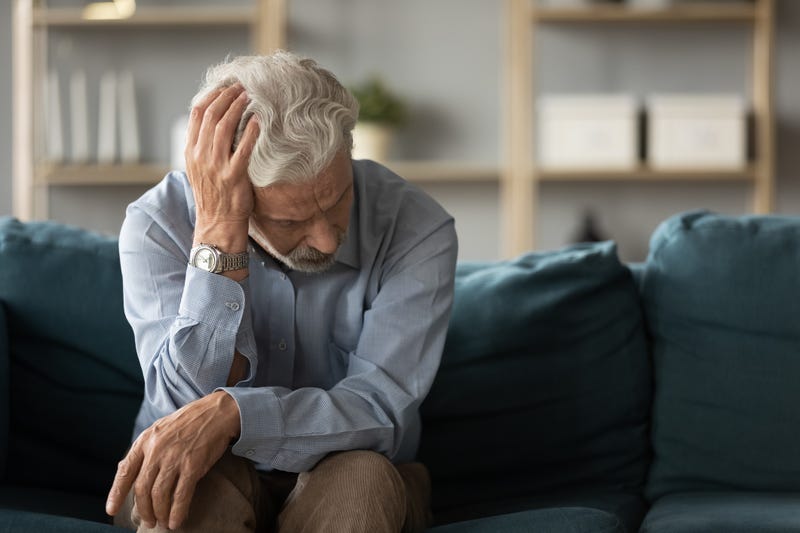 Frustrated unhappy middle aged mature man sitting on sofa, feeling depressed alone at home.