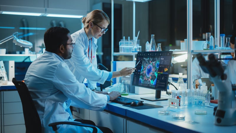 Female Research Scientist with Bioengineer Working on a Personal Computer with Screen Showing Virus Analysis Software