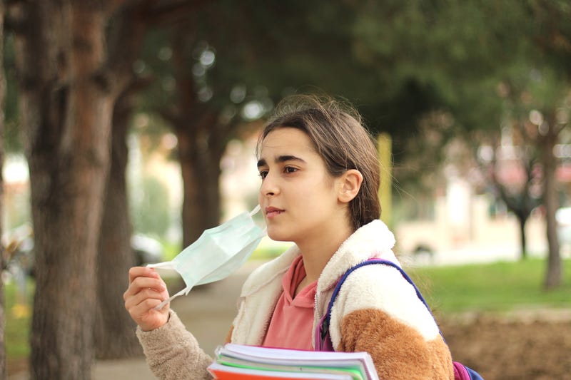 Young female student takes of protective face mask