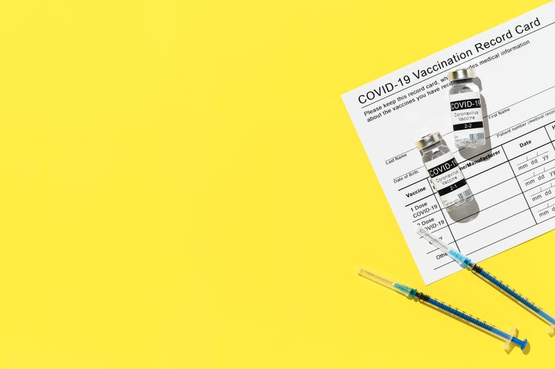 Coronavirus vaccination concept. Top view of vaccination record card, syringes, and two vials of the COVID-19 vaccine for two-stage injection. Bright yellow background