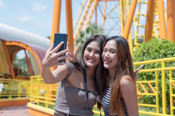 Girls take a selfie in front of a rollercoaster