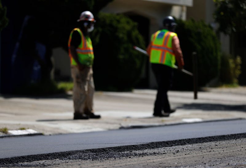Workers with the San Francisco Department of Public Works stand near freshly laid asphalt during a repaving project along 24th Avenue on April 08, 2021 in San Francisco, California.