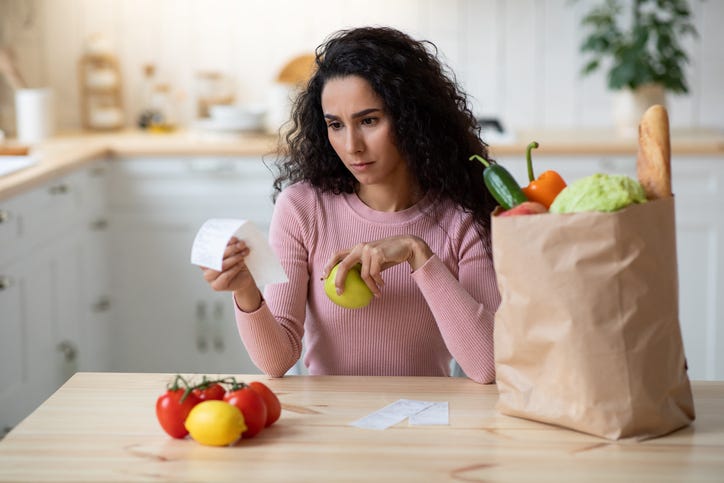 Concerned Young Woman Checking Bills In Kitchen After Grocery Shopping.
