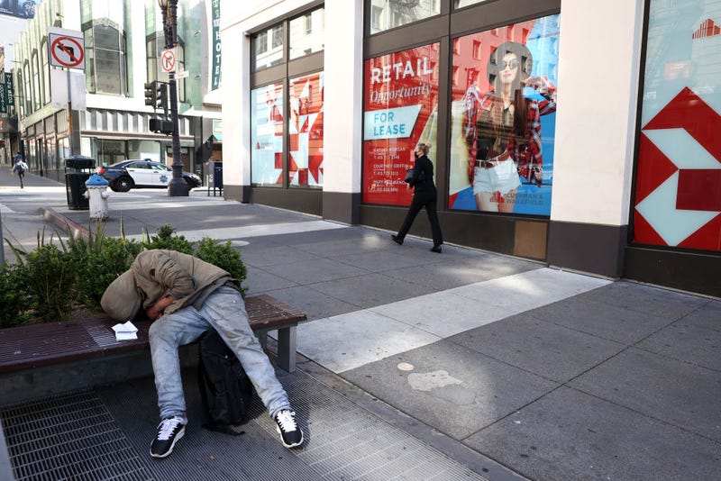 A homeless person sleeps on a bench in front of closed retail stores on April 16, 2021 in San Francisco, California.