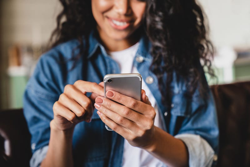 Smiling african american woman using smartphone at home, messaging or browsing social networks while relaxing on couch
