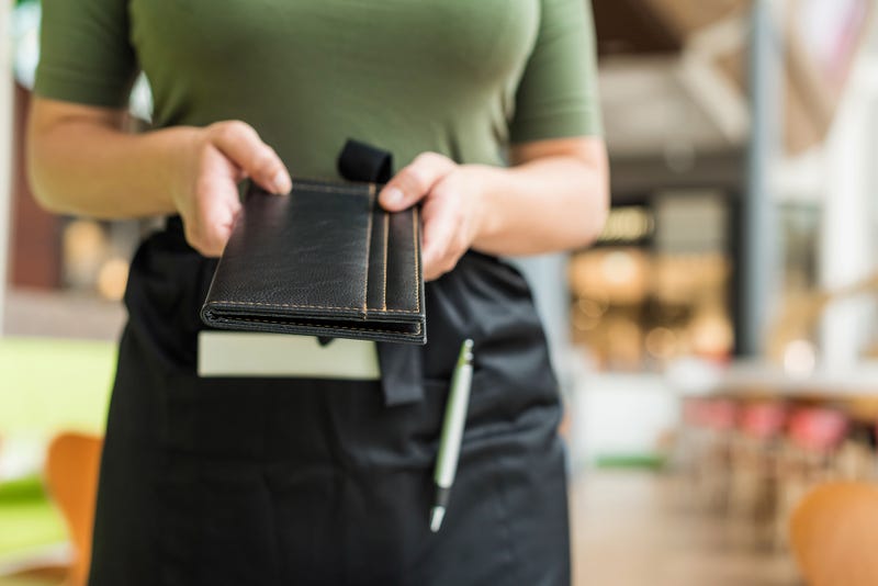 Waitress holding a bill folder, face cropped.