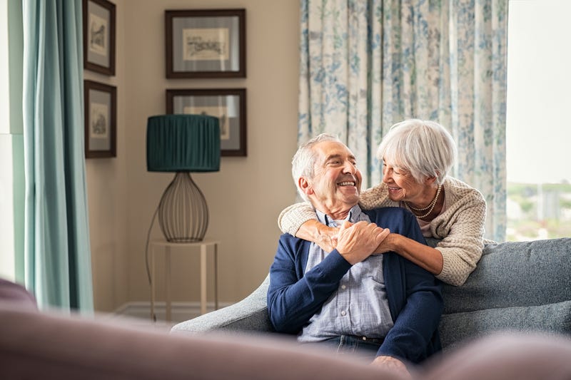 two old people sittng on couch holdinghands and smiling