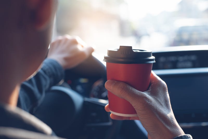 Man driver hand holding takeaway paper coffee cup while driving a car in the morning,