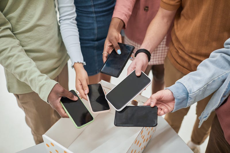 Top view closeup of diverse group of teenagers putting smartphones in box in no gadget classroom at school, copy space