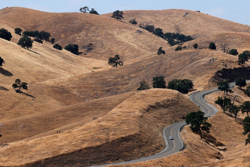 A car drives by hills covered with dry brown grass at the Eastman Lake Recreation Area on May 26, 2021 in Raymond, California.