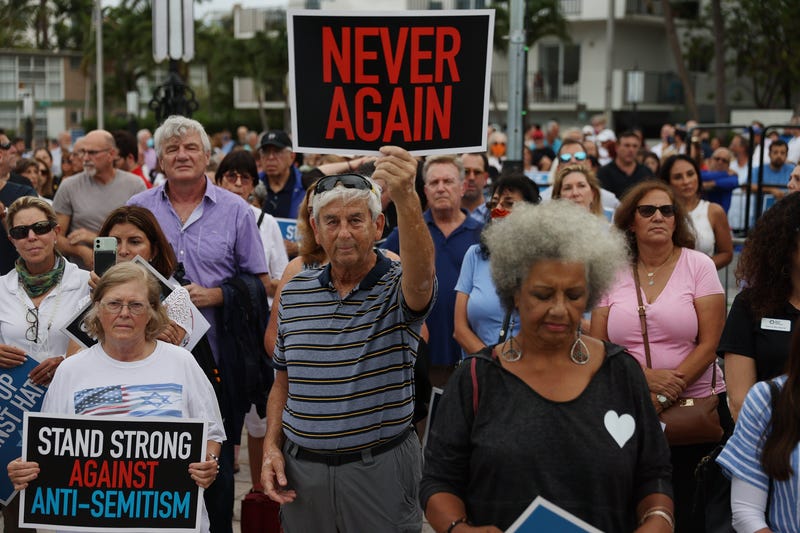 crowd of people, one man holds sign that says 'never again'