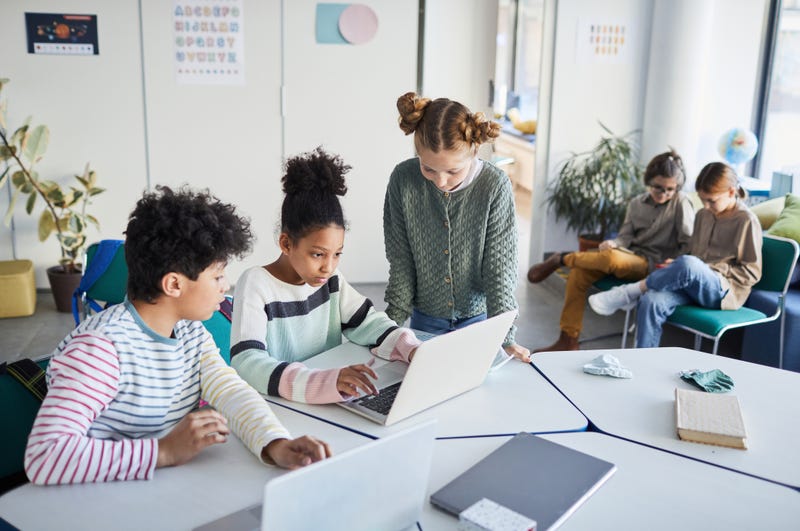 File - High angle view of a group of children working together at desk in classroom.