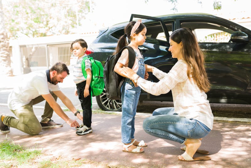 Side view of loving young parents smiling and saying goodbye to their little kids before sending them to school in the morning