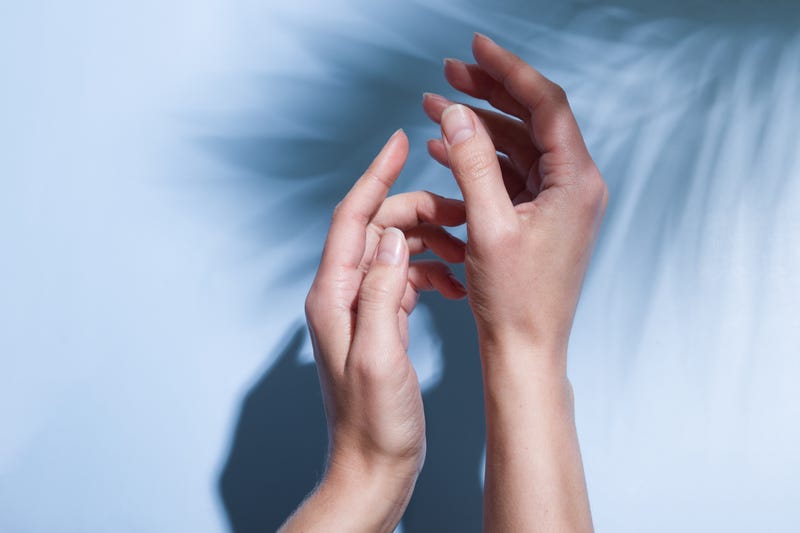 Beautiful female hands in sunlight on a blue background with the shadow of palm leaves