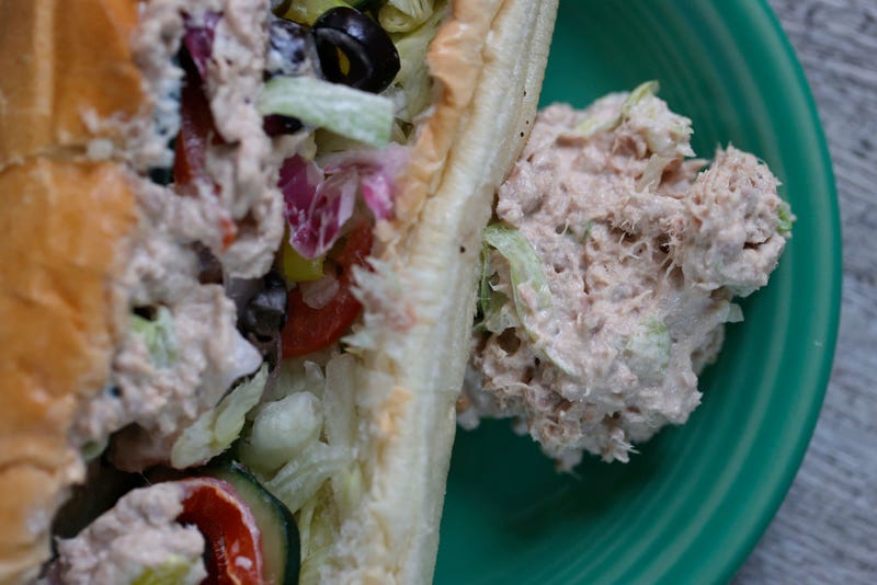 A scoop of tuna sits next to a tuna sandwich from Subway. 