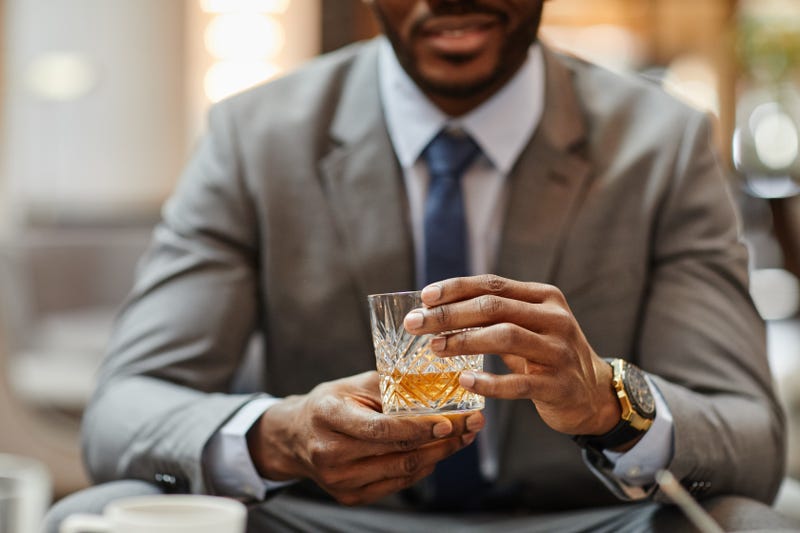 Cropped shot of successful African-American businessman enjoying glass of whiskey in hotel,