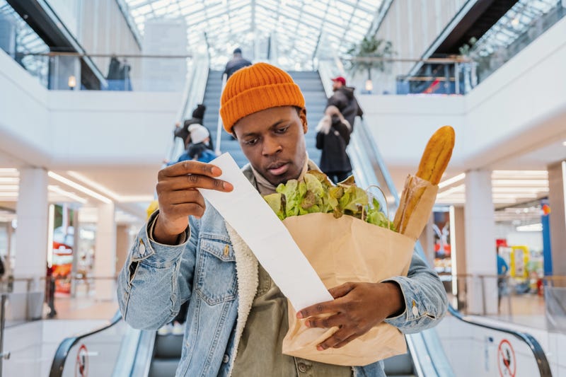 Black male holding bag of groceries and looking at receipt