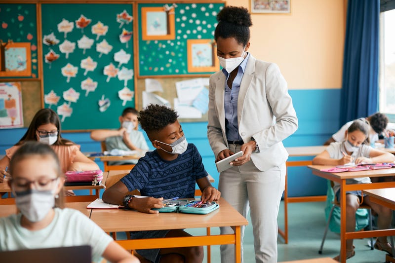 Teacher talks to student in classroom while wearing masks.