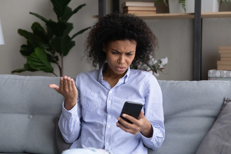 Unhappy young woman looks at smartphone screen confused by error or mistake online on device.